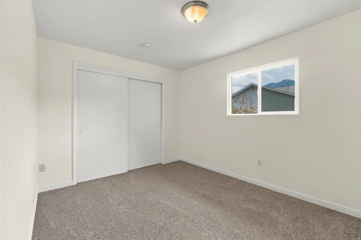 Neutral-toned bedroom featuring a dual-pane window, flush-mount ceiling light, built-in sliding door closet, and textured carpeting