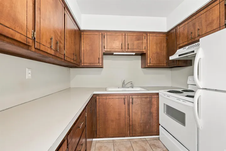 Kitchen featuring wood cabinetry, solid surface countertops, a white top-mount sink with chrome faucet, a white range, and a white refrigerator