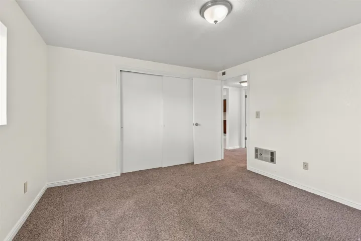 Carpeted interior room with white walls, a sliding door closet, and a semi-flush ceiling light fixture