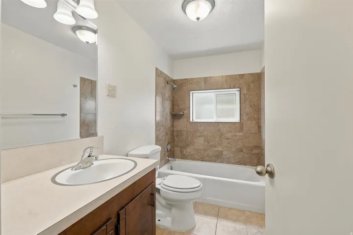 Bathroom featuring a white bathtub, ceramic tile shower surround, frosted window, and a vanity with a laminate countertop and undermount sink