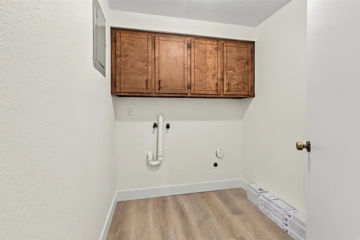 Laundry area featuring wood-finish flooring, white walls, and built-in wood cabinetry