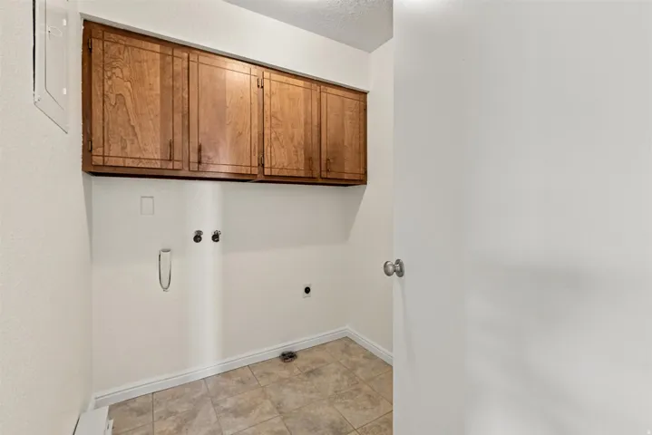 Utility space featuring upper wood cabinetry, neutral-toned tile flooring, and white baseboards