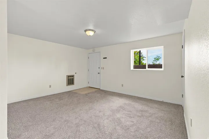 Carpeted room featuring a white door, a window with exterior visibility, a wall-mounted vent, a ceiling-mounted light fixture, and light-colored walls