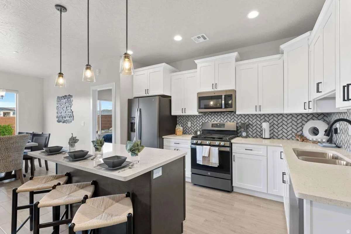 Modern kitchen featuring an island with pendant lighting, white shaker-style cabinetry, stainless steel appliances, herringbone tile backsplash, and light-toned countertops