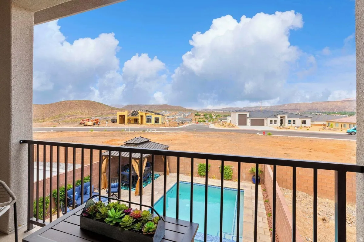Private balcony featuring black metal railing, overlooking a rectangular swimming pool with paved surround