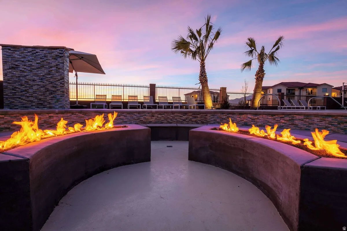 Curved fire pit design, stone veneer wall accents, concrete hardscaping, mature palm trees, and perimeter fencing