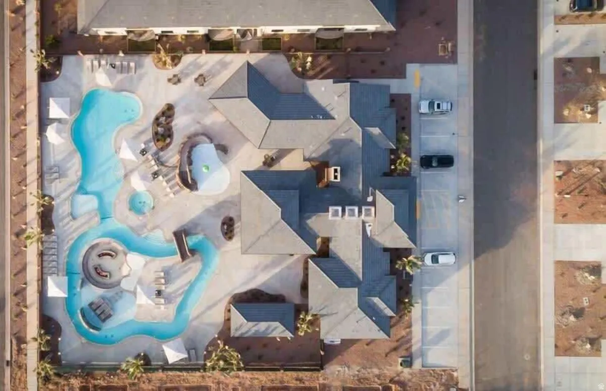 Expansive amenity area featuring multiple pools with a water slide, shaded lounging areas, and a central building with gray shingle roofing