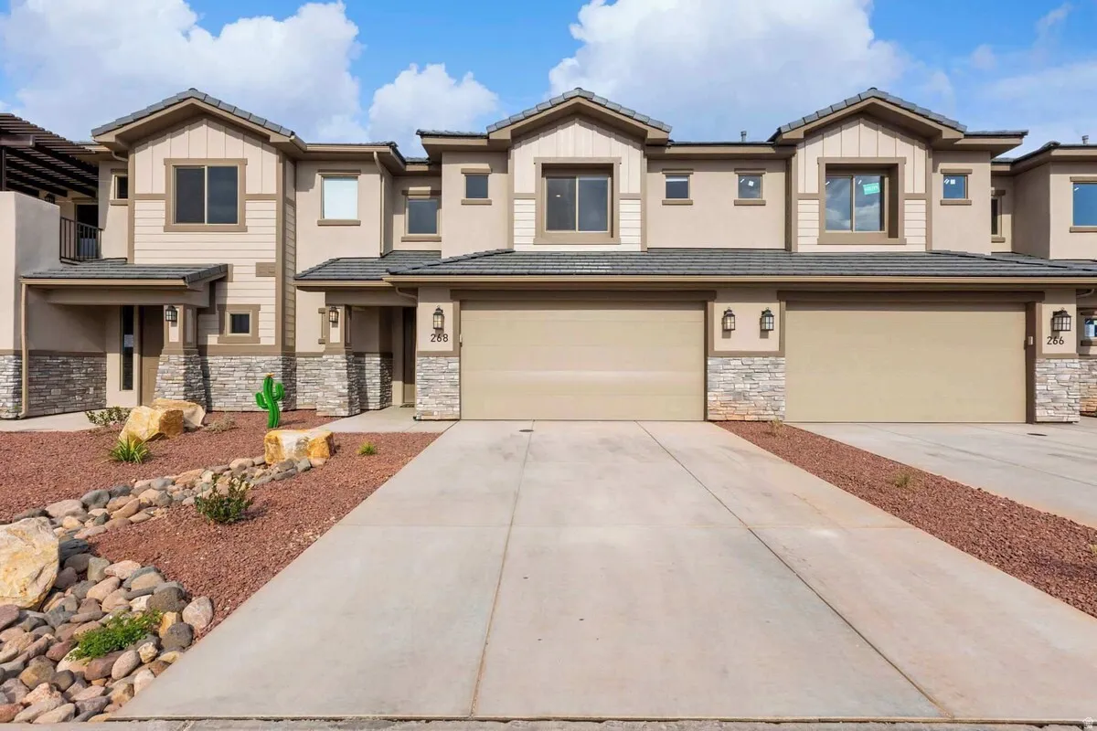 Contemporary stucco and stone-clad townhouse featuring multiple garage doors, concrete driveways, and low-maintenance xeriscaping with decorative rock