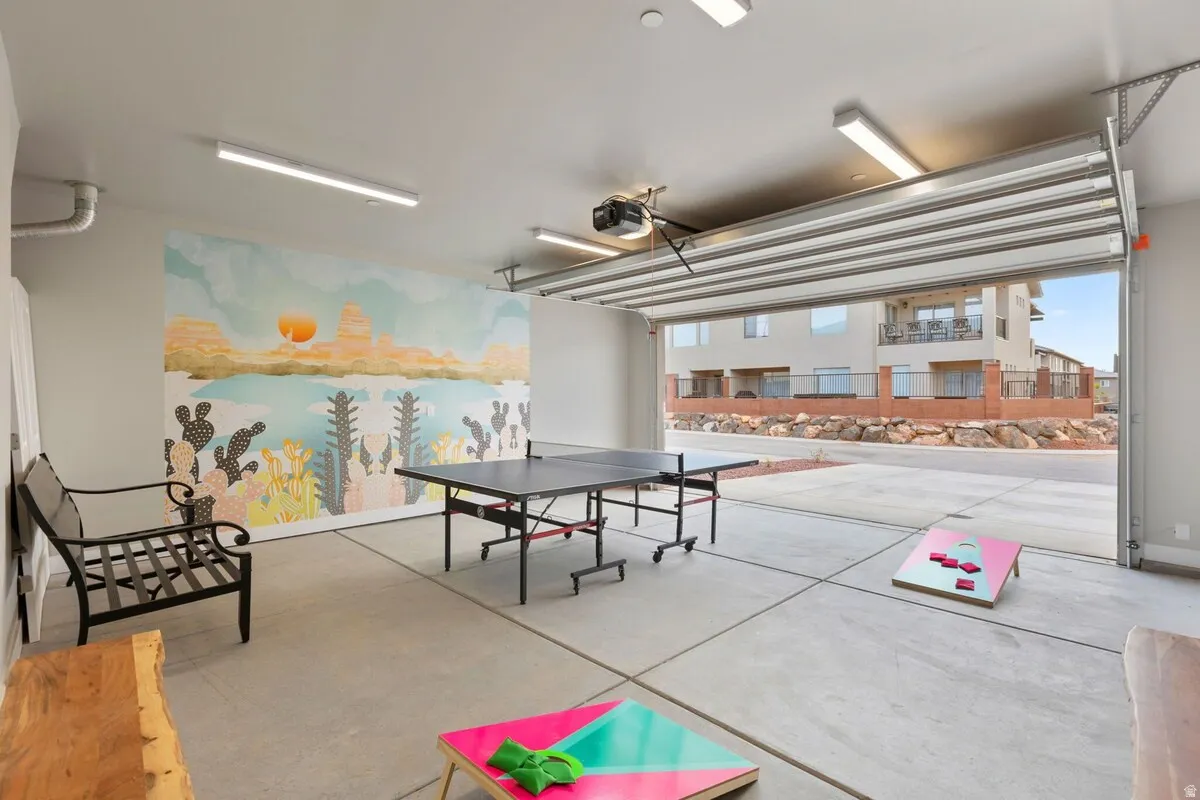 Spacious garage with concrete flooring, overhead lighting, an expansive wall mural, and an open overhead door