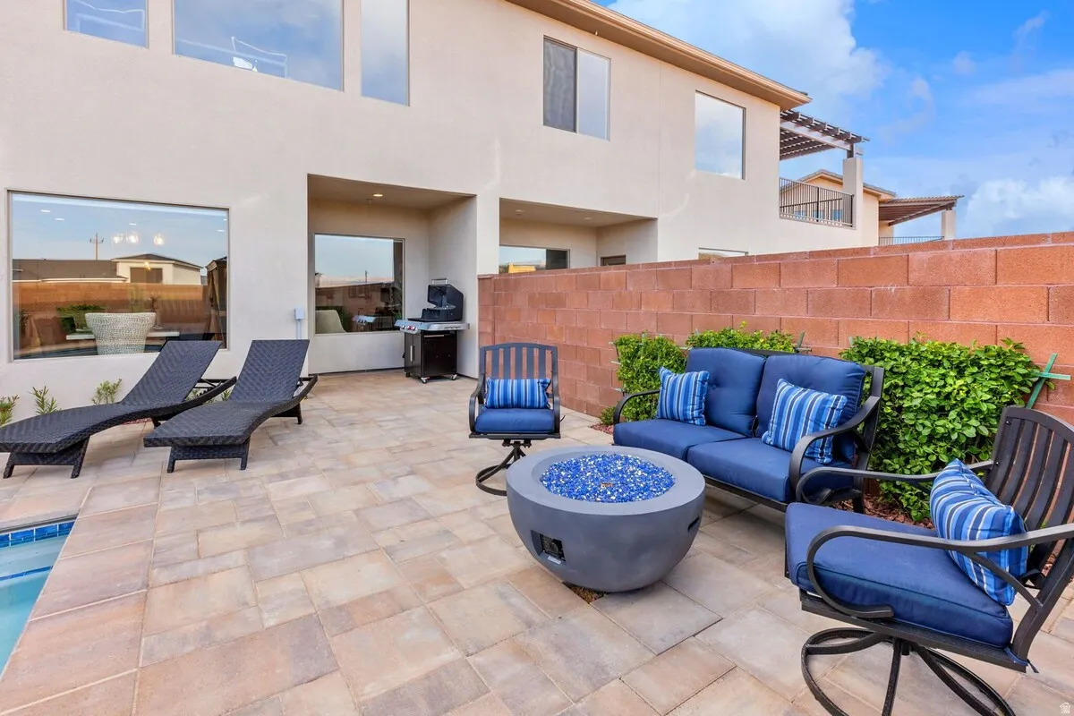 Expansive paver patio with a built-in fire pit, rectangular swimming pool, and a block retaining wall