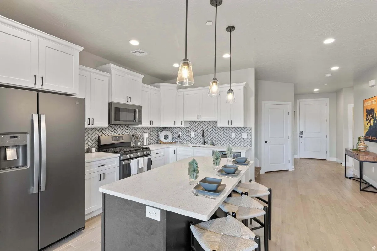 Contemporary kitchen featuring a large island with seating, white shaker-style cabinetry, stainless steel appliances, and a herringbone tile backsplash