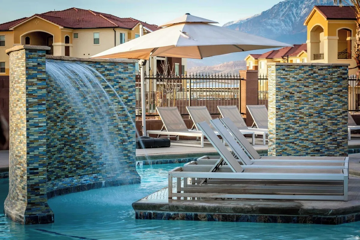Resort-style pool area featuring a waterfall with mosaic tile surround, spacious tanning ledge, and multiple chaise lounges