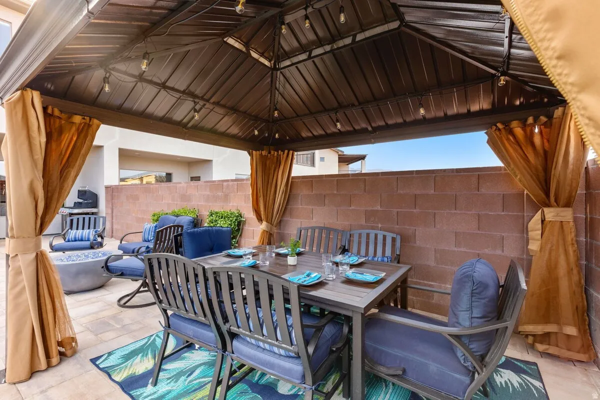 Covered patio featuring a metal gazebo with string lighting, privacy curtains, and a paver stone surface