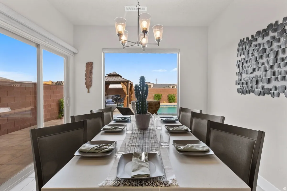Dining area featuring a modern chandelier, large window overlooking a pool, and sliding glass door to an outdoor patio