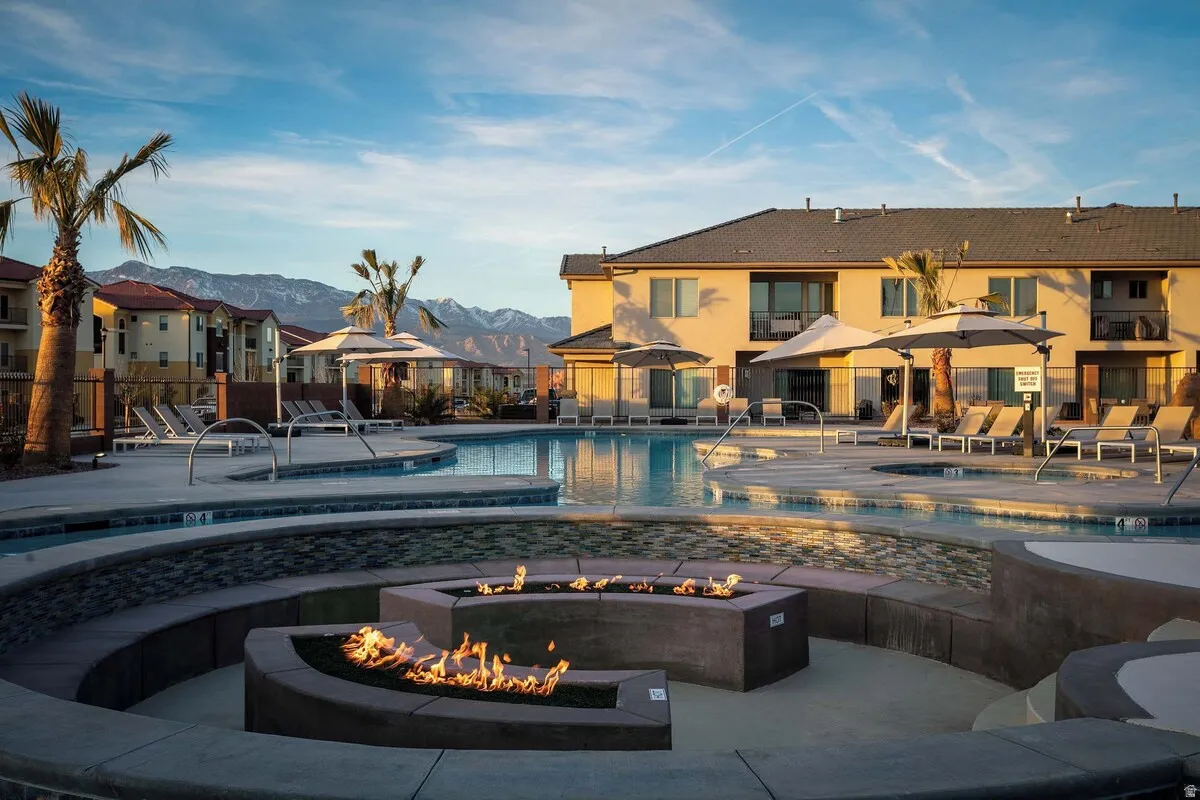 Expansive pool deck featuring a geometric fire pit with built-in seating, multiple lounge areas, and mature palm trees