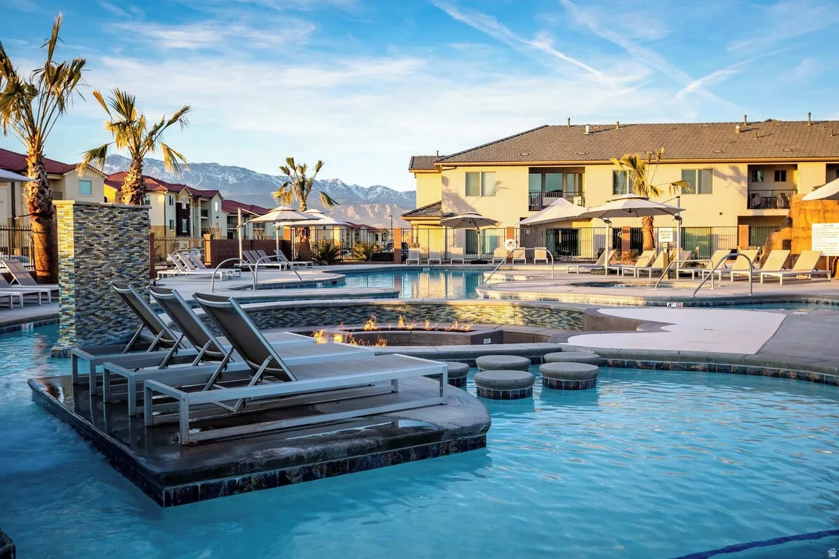 Expansive swimming pool area featuring integrated lounge seating, multiple water features, and a built-in fire pit
