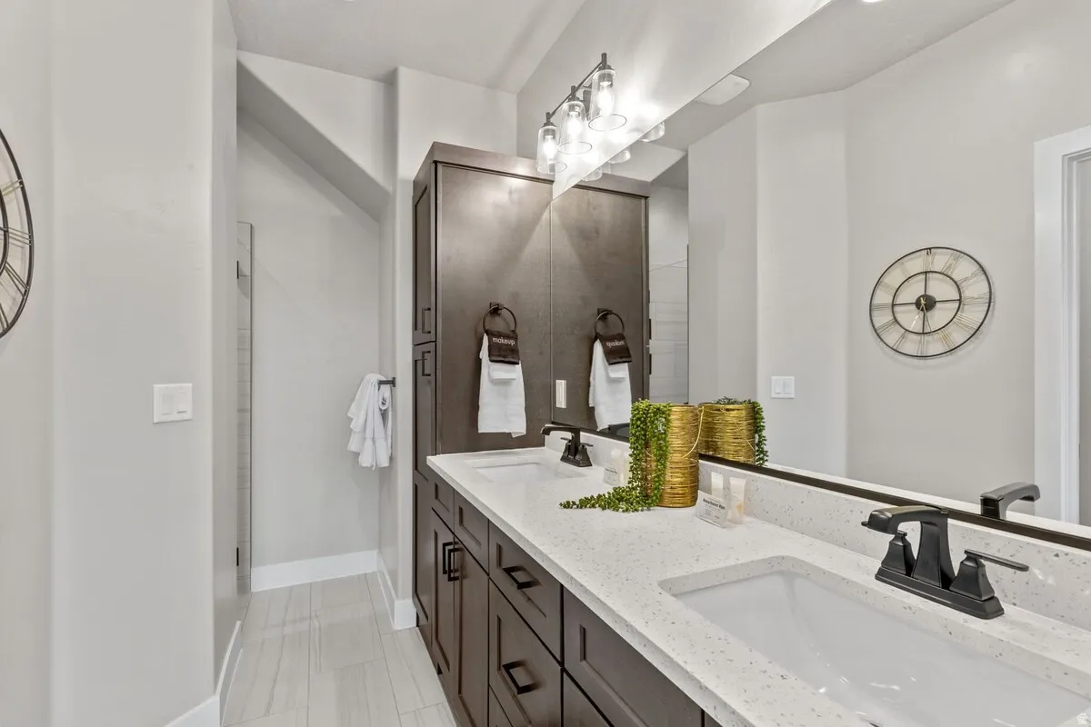 Bathroom featuring a double vanity with white speckled countertops, dark wood-finish cabinetry, and matte black fixtures
