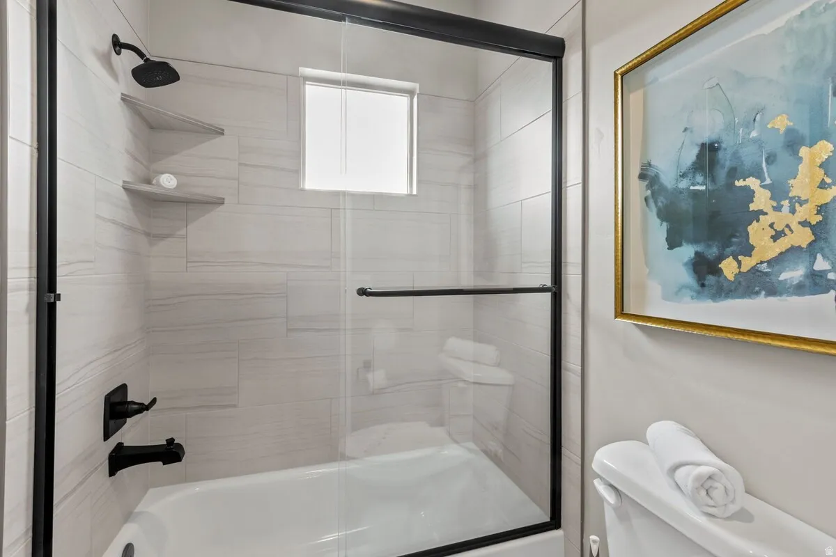 Bathtub with glass enclosure and matte black fixtures, featuring white tiled walls with integrated corner shelves and an overhead window