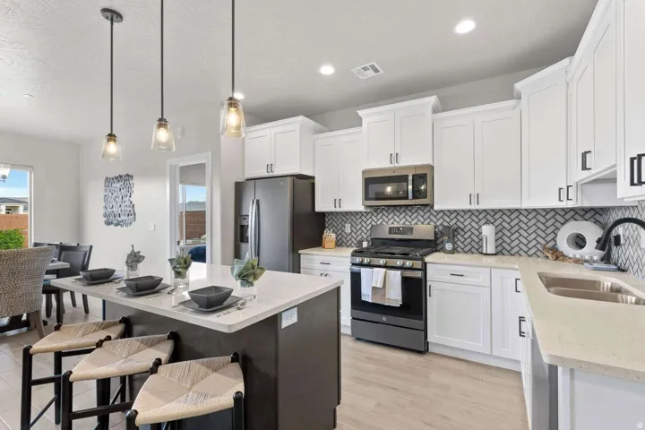 Modern kitchen featuring an island with pendant lighting, white shaker-style cabinetry, stainless steel appliances, herringbone tile backsplash, and light-toned countertops