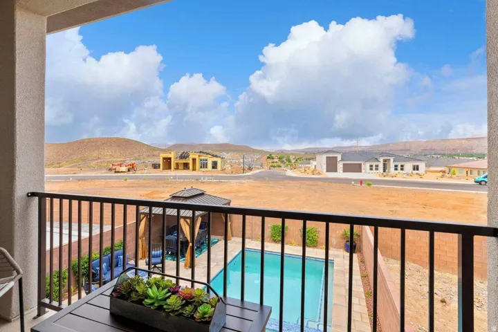 Private balcony featuring black metal railing, overlooking a rectangular swimming pool with paved surround