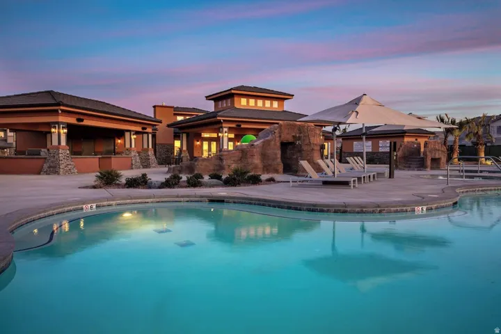 Resort-style pool area featuring a large swimming pool, textured rock-finish water features, a shaded lounge area with deck chairs, and a covered outdoor entertainment space with built-in stone accents