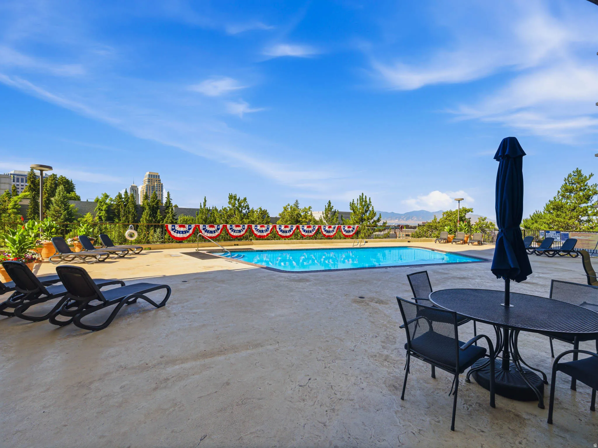 Outdoor swimming pool with a concrete surround, lounge chairs, and a dining area with an umbrella