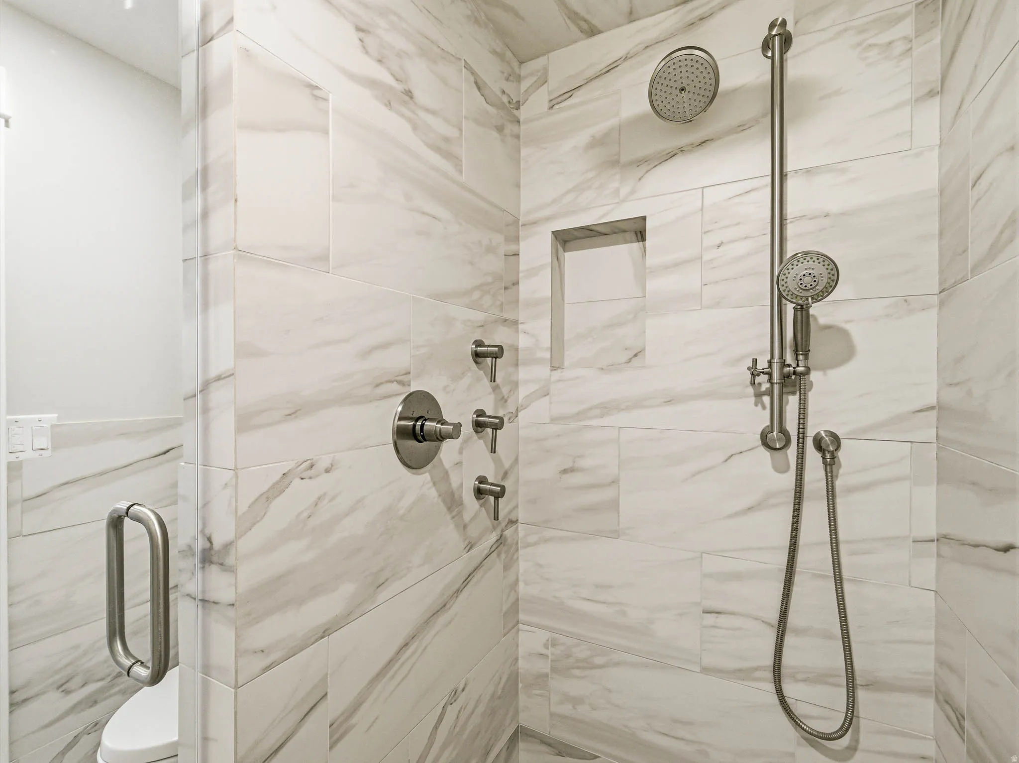 Walk-in shower featuring large format marble-look tile, rain shower head, handheld shower fixture, recessed niche, and brushed nickel hardware