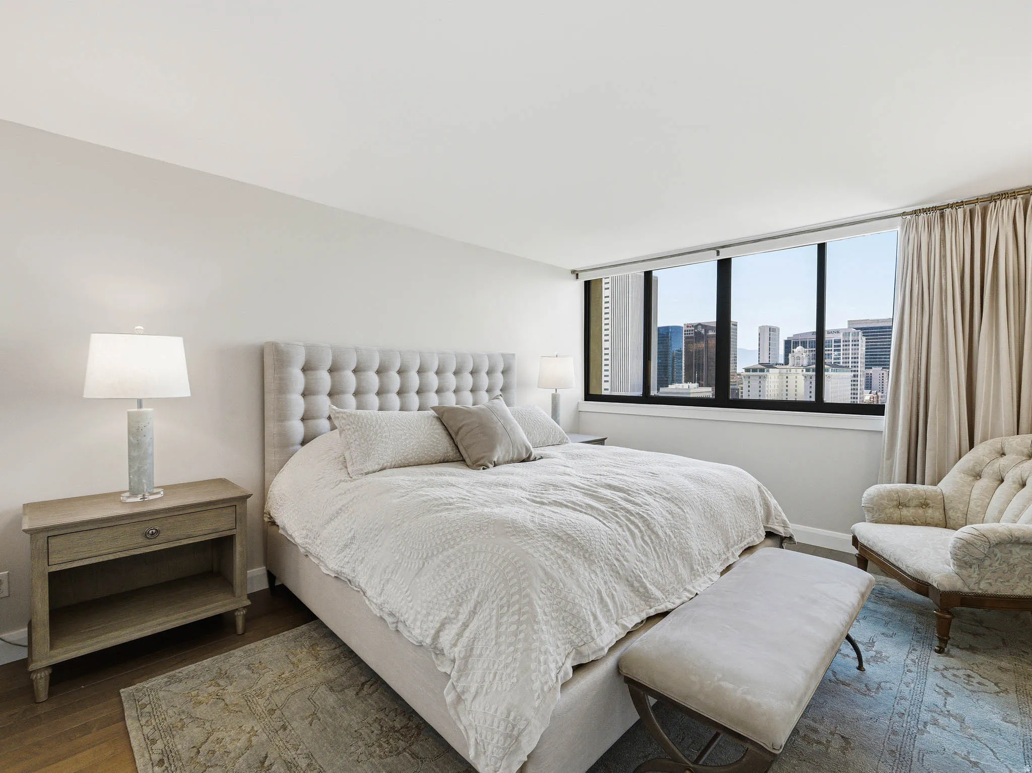 Bedroom featuring expansive windows with city buildings visible, light wood-finish flooring, and a neutral color palette