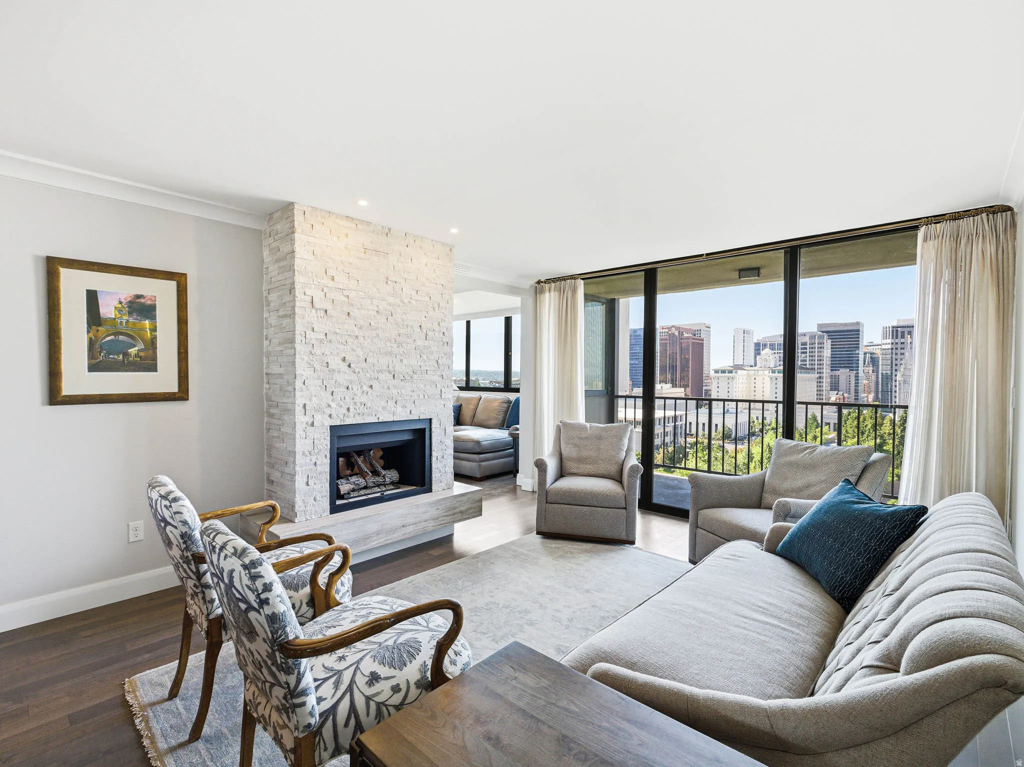 Spacious living area featuring a stacked stone fireplace, large glass panel balcony access, wood-finish flooring, recessed lighting, and crown molding