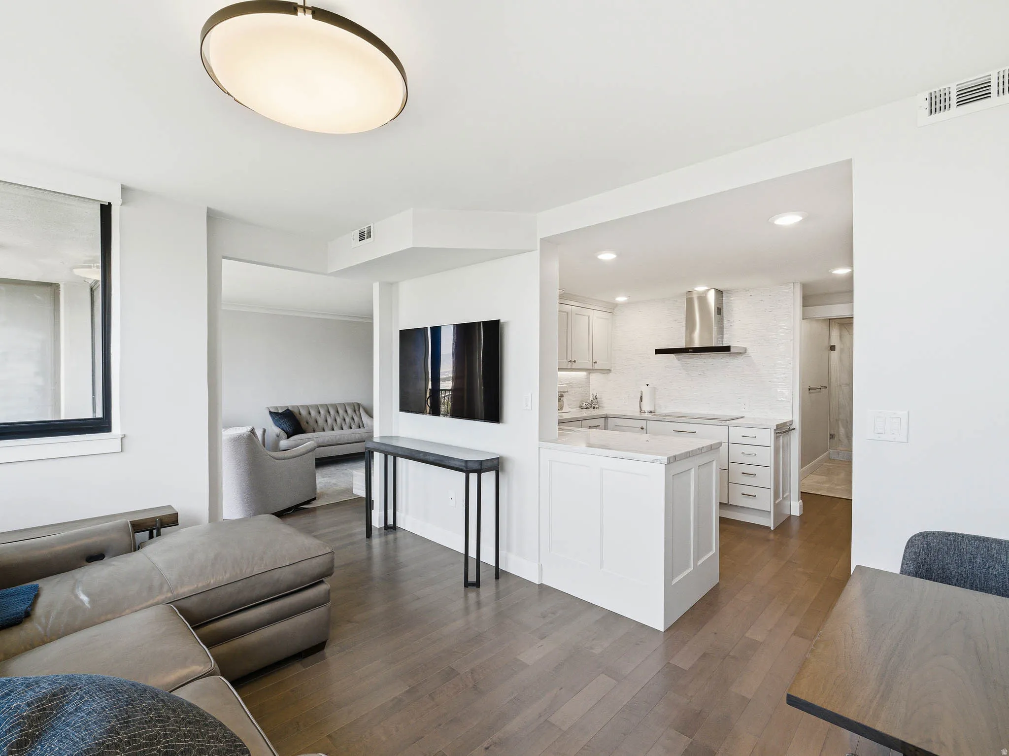 Open-concept living space featuring wood-finish flooring throughout, a modern kitchen with white cabinetry and stainless steel appliances, and recessed lighting
