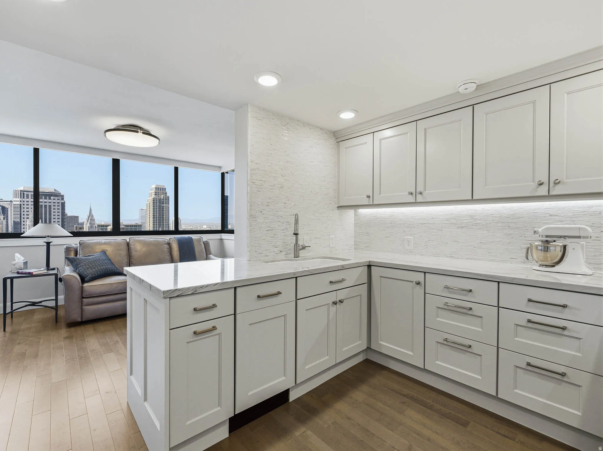 Modern kitchen featuring light gray cabinetry with brushed nickel hardware, white stone countertops, and a full-height tiled backsplash