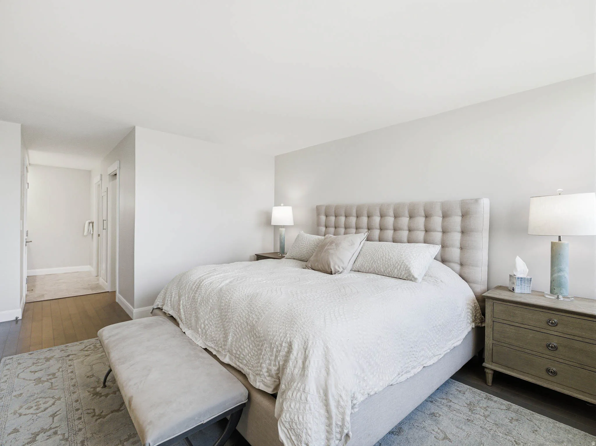 Spacious sleeping area featuring hardwood flooring, light neutral wall tones, and a plush upholstered headboard