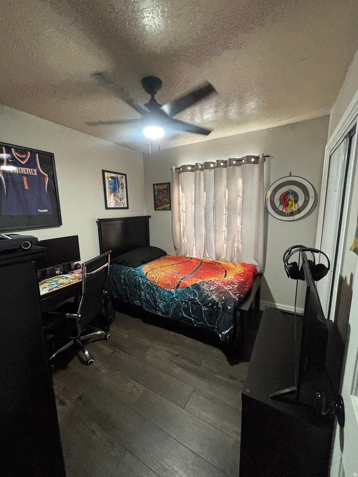 Spacious room featuring wood-finish flooring, a ceiling fan with integrated lighting, and a window with curtain rods