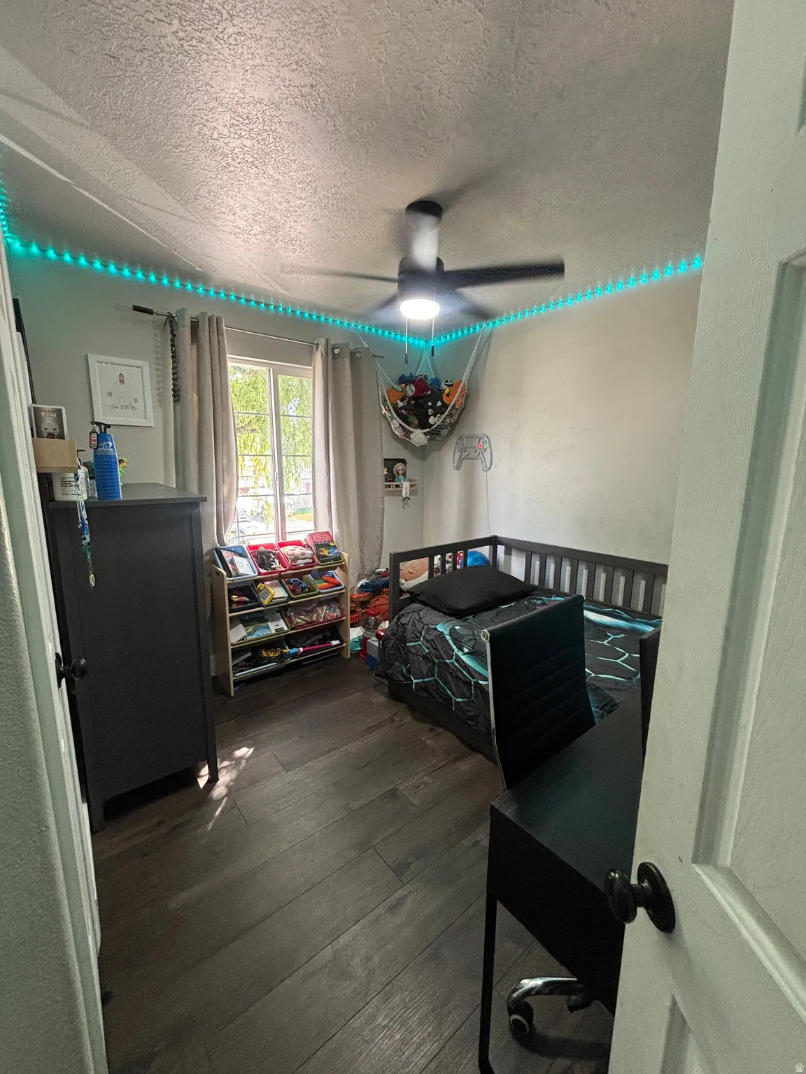 Room featuring wood-finish flooring, a ceiling fan with integrated lighting, and a window with curtains