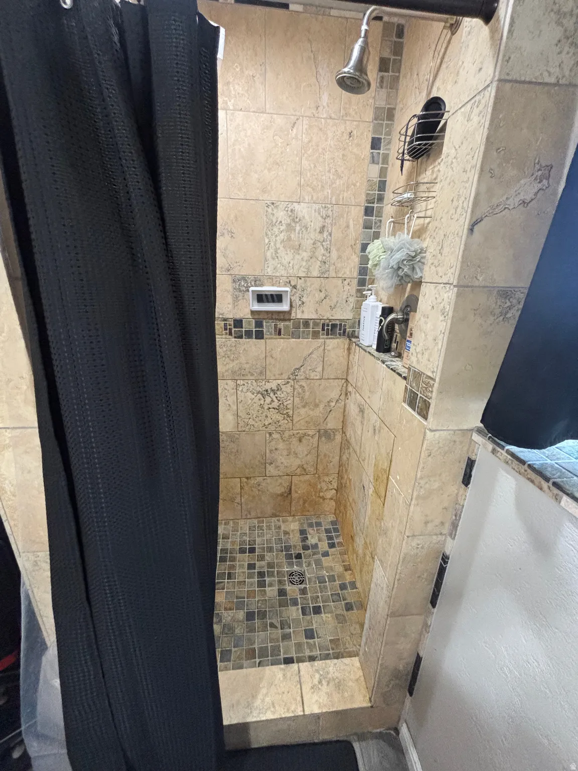 Tiled shower stall featuring a mosaic tile floor, coordinated wall tiles, and a recessed niche