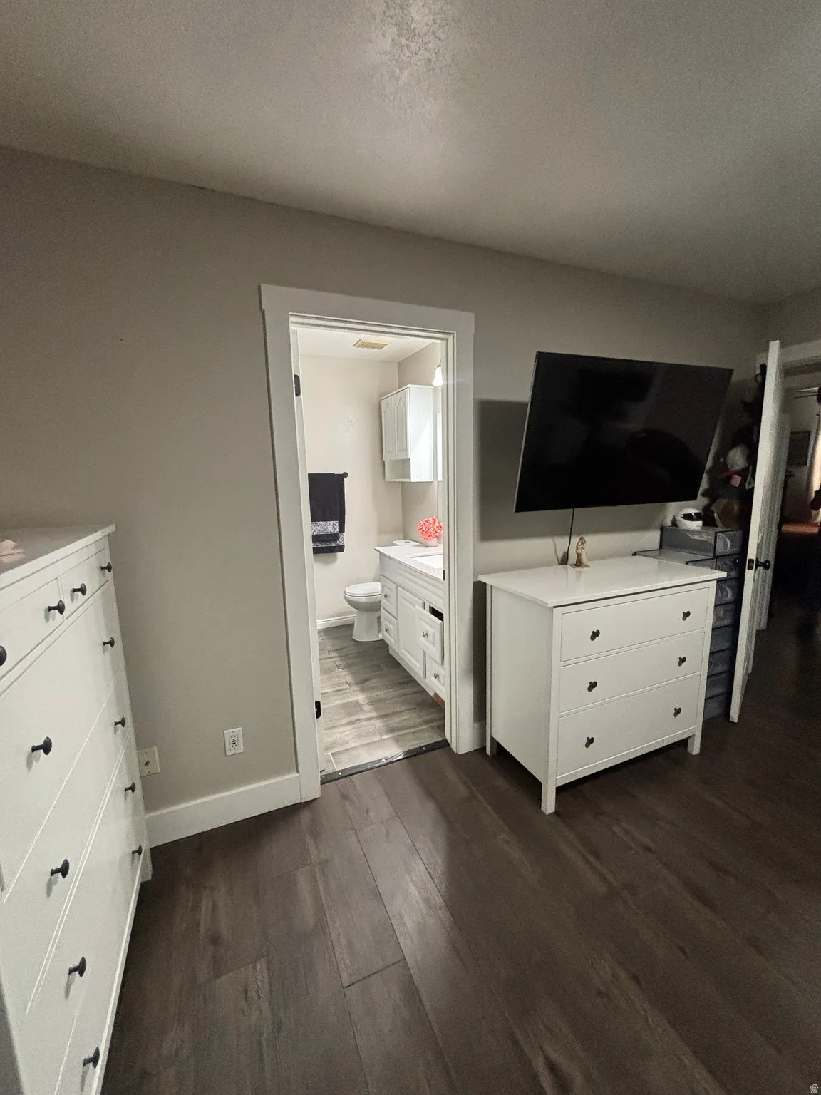 Dark wood-finish flooring extending into a bathroom with white vanity cabinetry and wood-look tile flooring