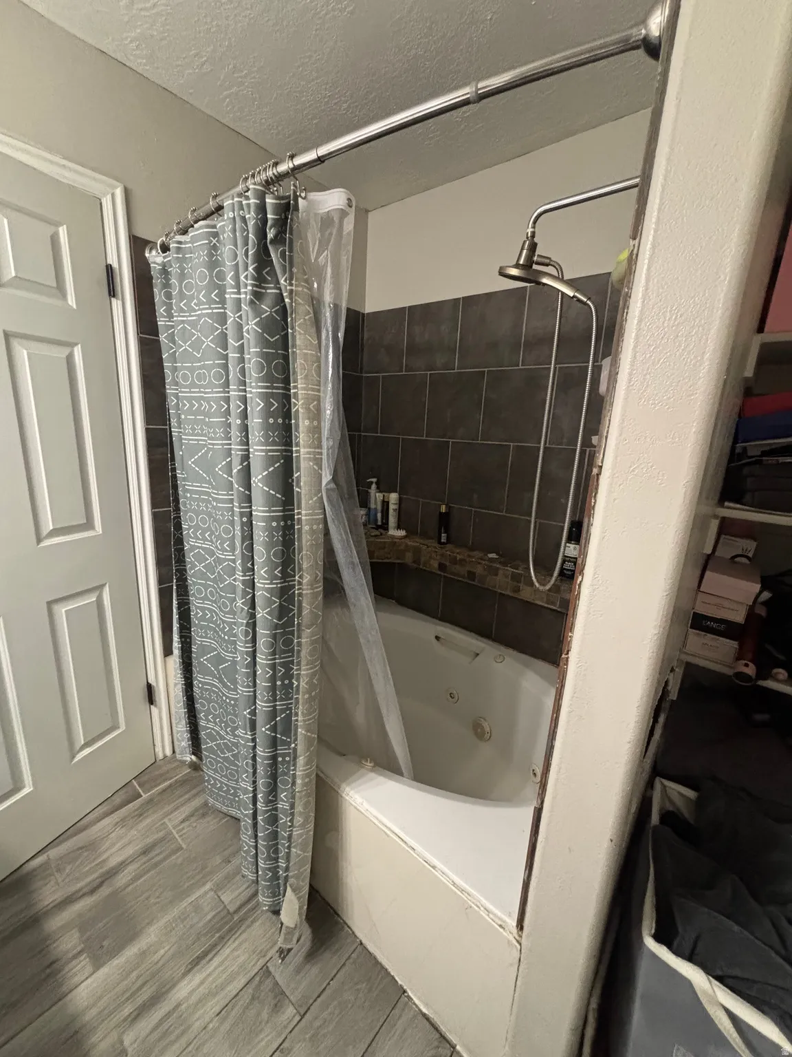 Bathroom featuring a jetted tub, dark tiled surround with decorative accent tile, and a bronzed shower head