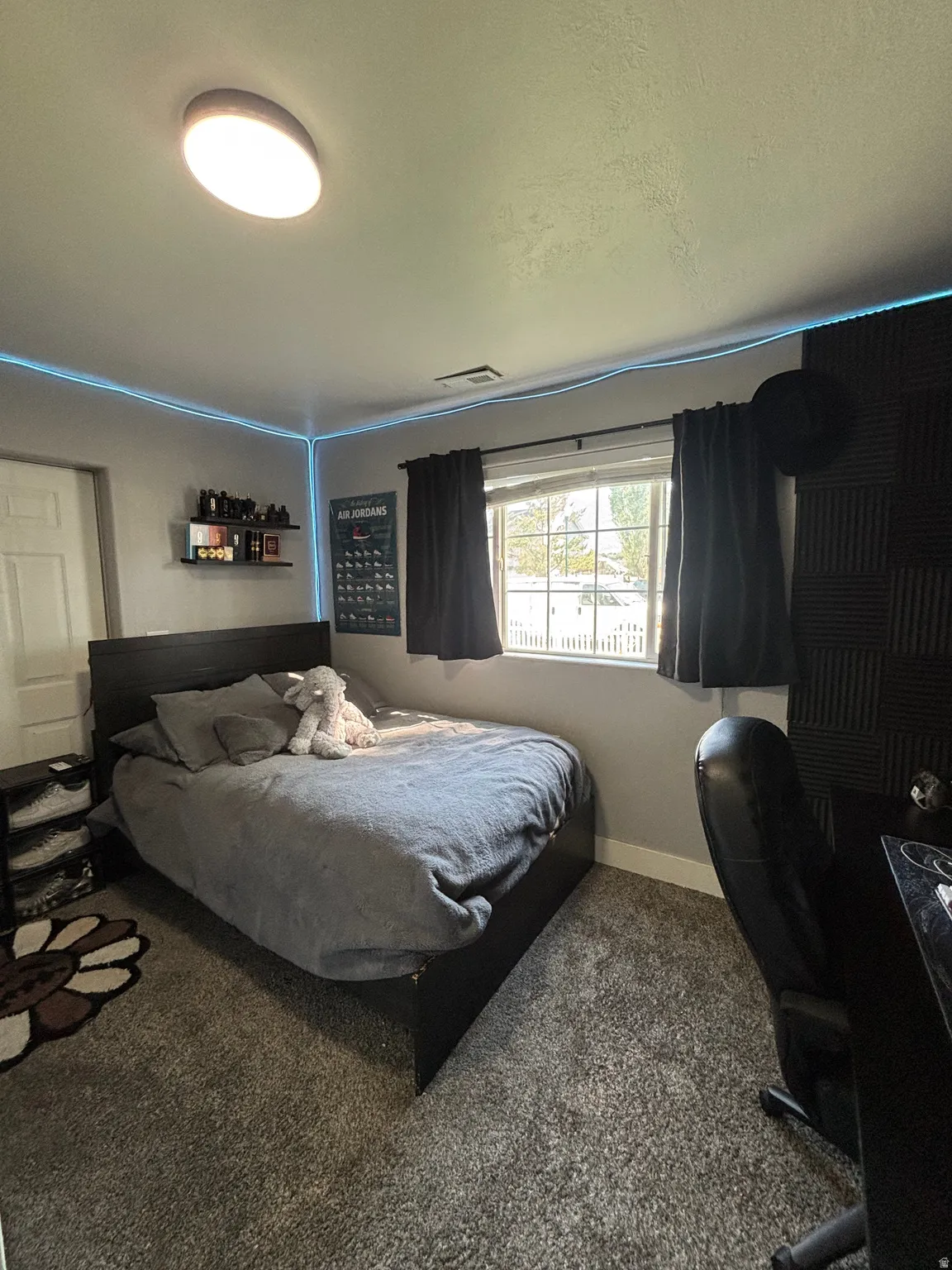 Bedroom featuring a window with dark curtains, light gray walls, and textured gray carpeting