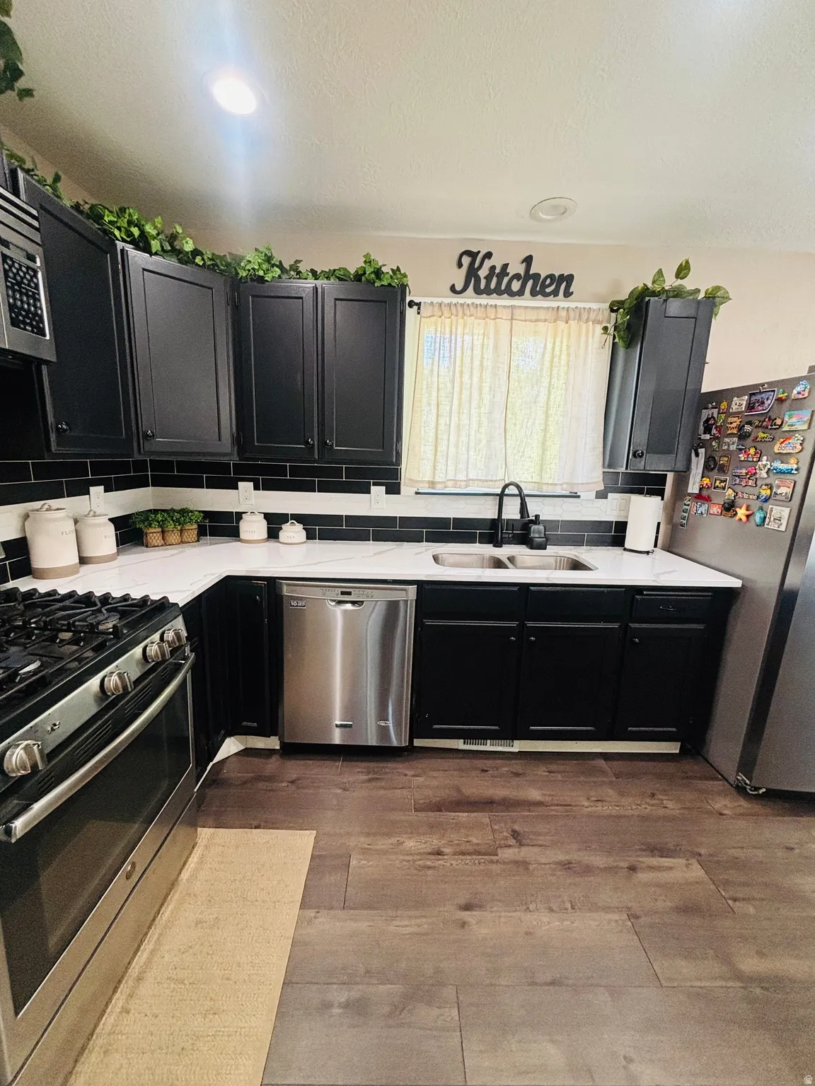 Kitchen featuring black cabinetry, white countertops, stainless steel appliances, and wood-finish flooring