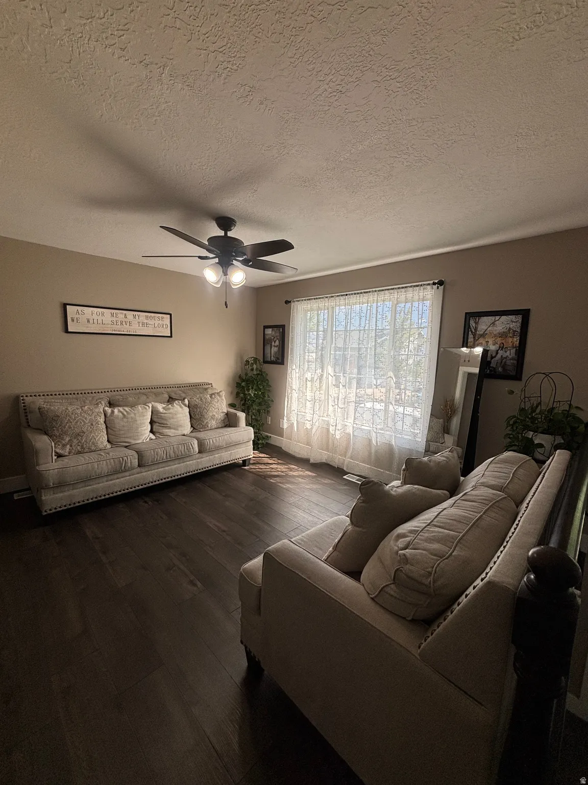 Spacious interior featuring dark wood-finish flooring, a ceiling fan with integrated lighting, and a large window with sheer white curtains