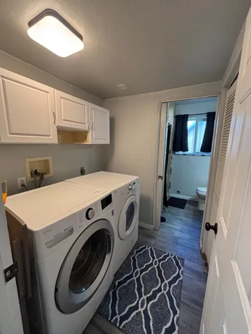 Dedicated laundry area featuring white upper cabinetry, wood-finish flooring, and overhead lighting