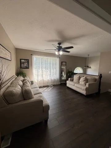 Spacious living area featuring wood-finish flooring, a vaulted ceiling, and a ceiling fan with integrated lighting