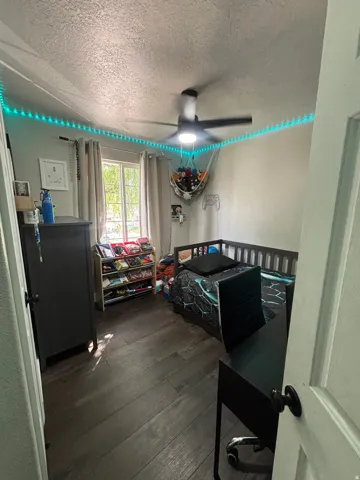 Room featuring wood-finish flooring, a ceiling fan with integrated lighting, and a window with curtains