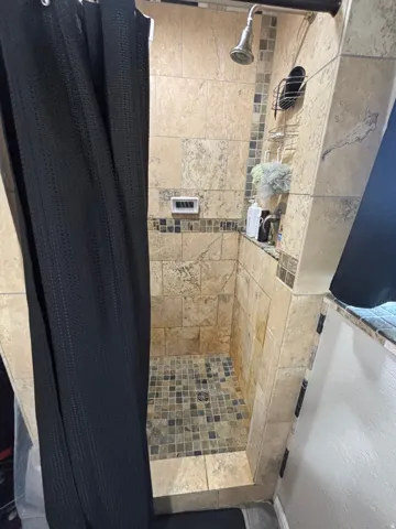 Tiled shower stall featuring a mosaic tile floor, coordinated wall tiles, and a recessed niche