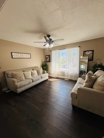 Spacious room featuring dark wood-finish flooring, a large window with white sheer coverings, and neutral-toned walls