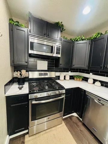 Kitchen featuring black cabinetry, stainless steel appliances, a gas range, white countertops, and a black subway tile backsplash