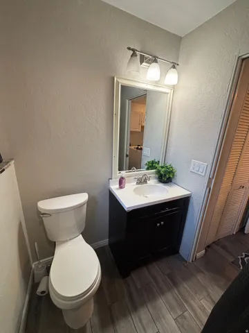 Bathroom featuring a white toilet, dark wood-finish vanity with a white countertop and integrated sink, a framed mirror, and a three-light vanity fixture