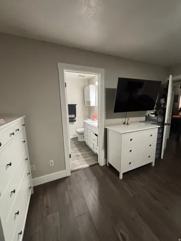 Dark wood-finish flooring extending into a bathroom with white vanity cabinetry and wood-look tile flooring