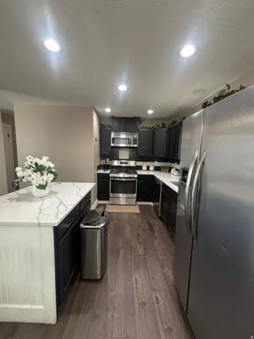 Kitchen featuring dark cabinetry, stainless steel appliances, a center island with a stone countertop, wood-finish flooring, and recessed lighting