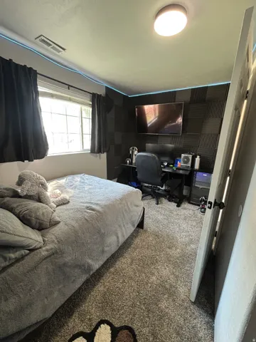 Bedroom featuring light gray carpeting, a window with dark drapes, and a ceiling-mounted light fixture